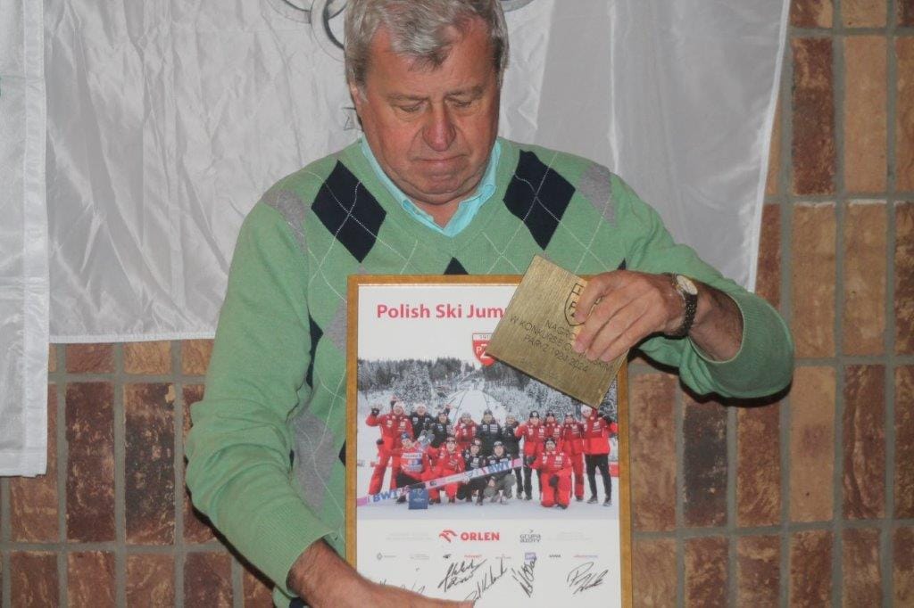 Mężczyzna trzyma nagrodę i plakat narciarski.