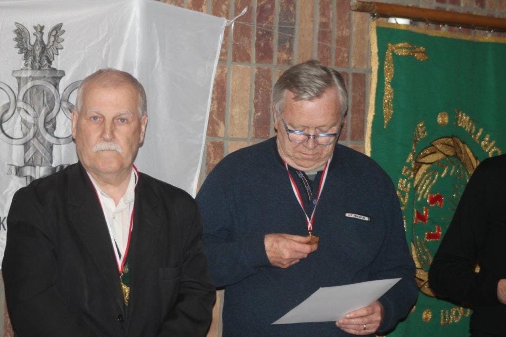 Dwaj starsi mężczyźni z medalami przy banerze z orłem