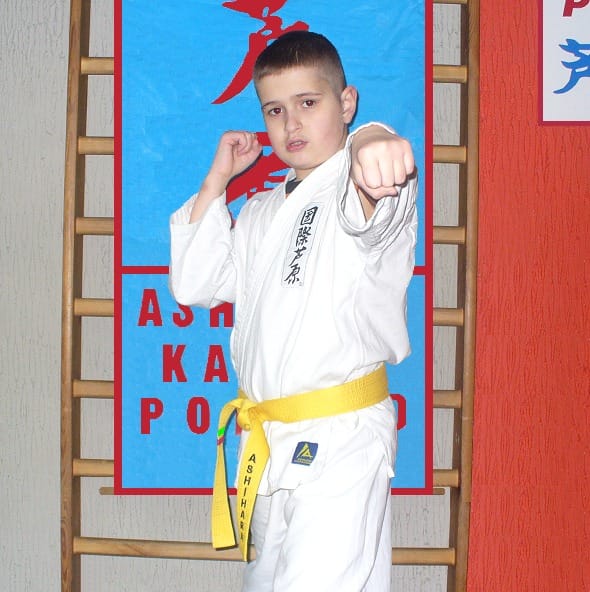 Dziecko w karate gi z żółtym pasem pozujące do zdjęcia