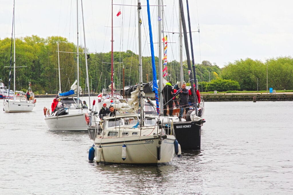 Żaglówki z załogami na spokojnej rzece, las w tle