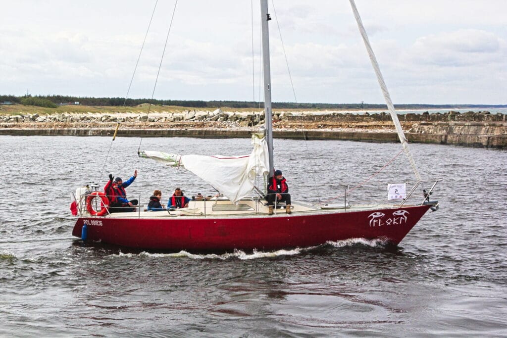 Czerwony żaglówka z załogą na tle falochronu