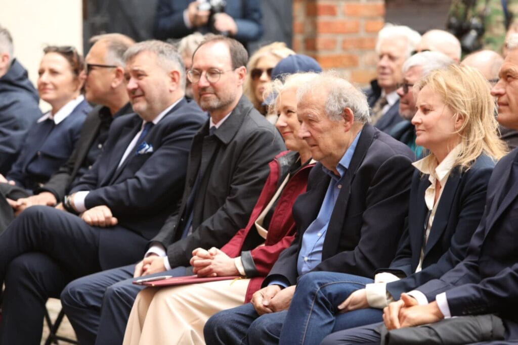 Grupa osób siedzi na uroczystości na zewnątrz