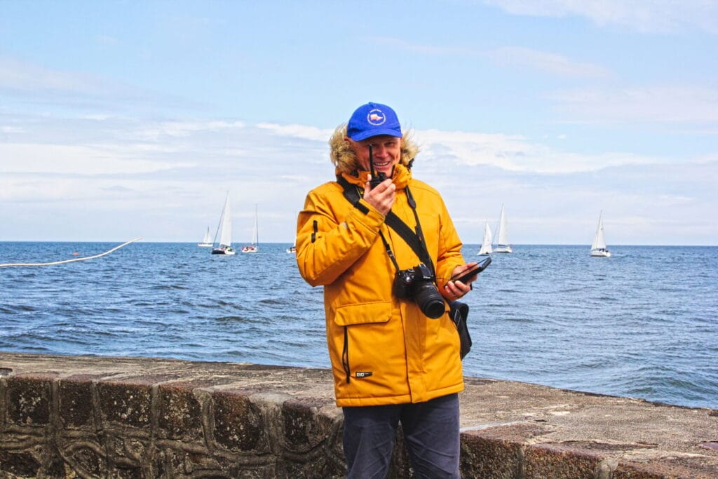 Mężczyzna w żółtej kurtce robi zdjęcia nad morzem