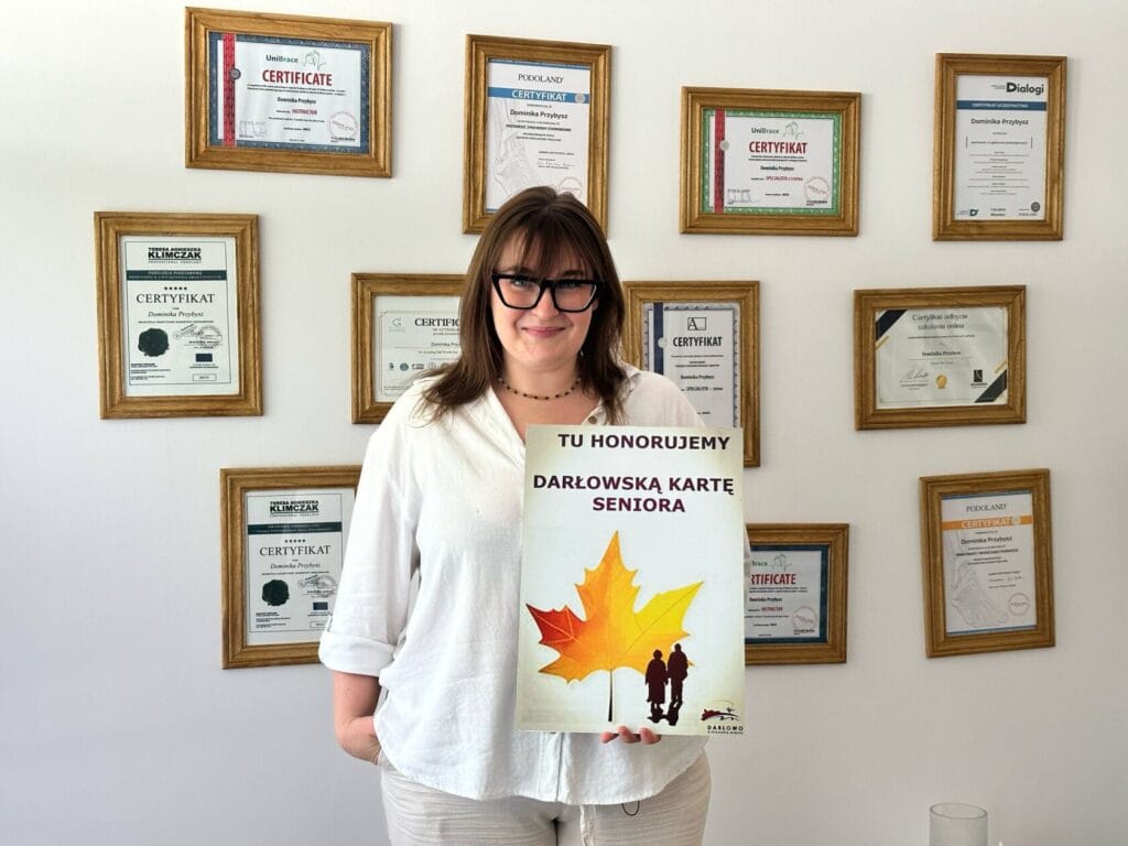 Kobieta prezentująca certyfikat otoczona innymi dyplomami