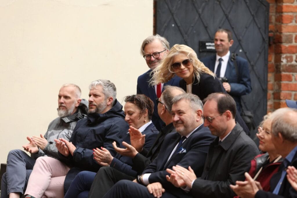 Grupa osób w garniturach oklaskuje na zewnątrz