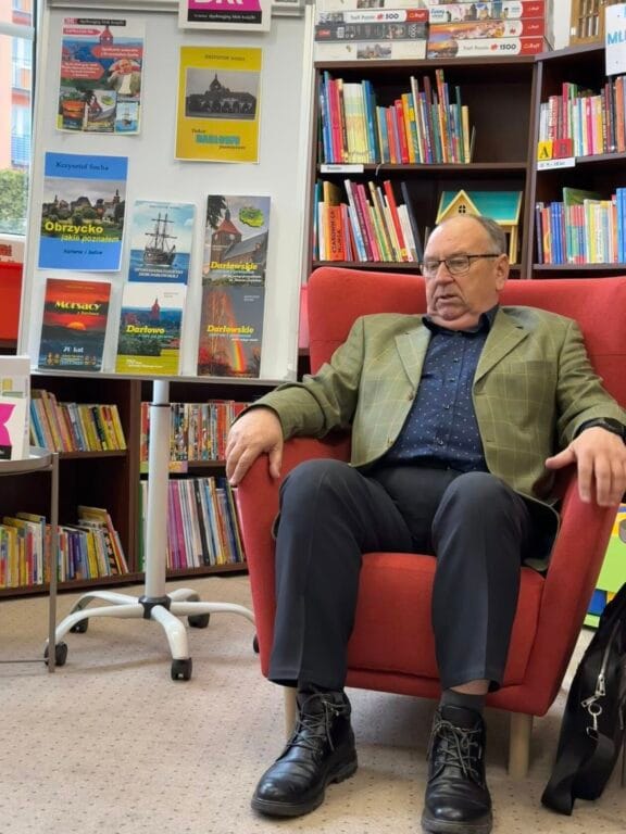 Starszy mężczyzna siedzi w czerwonym fotelu w bibliotece