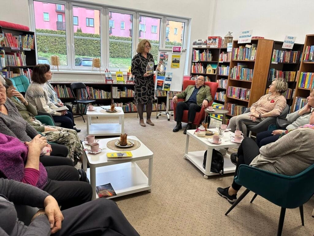 Spotkanie seniorów w bibliotece, kobieta prezentuje książkę