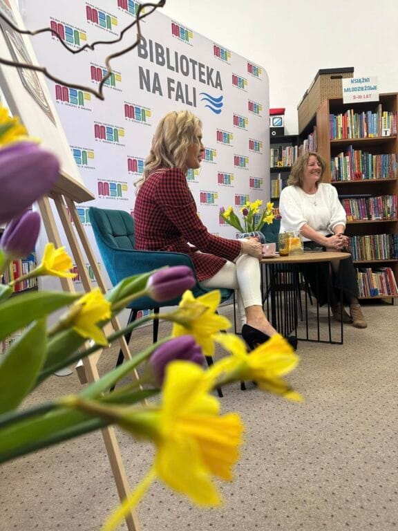 Dwie kobiety dyskutują w bibliotece, kwiaty na pierwszym planie