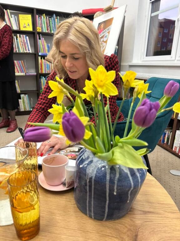 Kobieta czyta przy stole z żółtymi i fioletowymi kwiatami