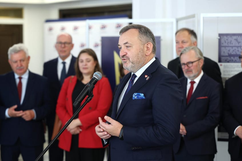 Mężczyzna przemawiający, grupa ludzi w tle, konferencja