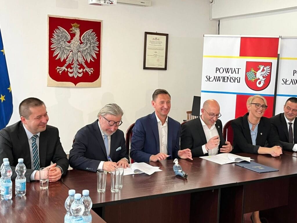 Osoby podpisujące dokumenty w urzędzie, godło Polski w tle