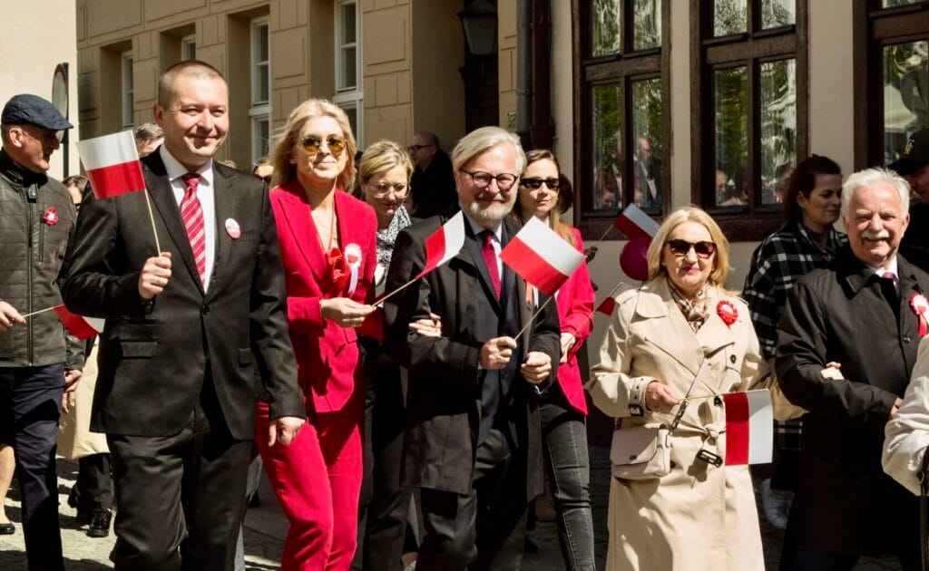 Grupa osób niesie polskie flagi na uroczystości