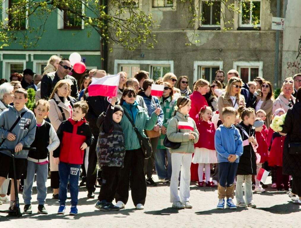 Grupa osób obserwuje paradową uroczystość na ulicy