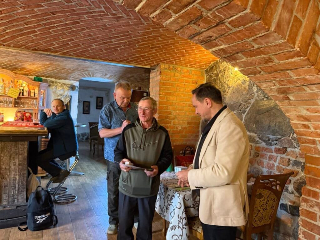 Trzej mężczyźni w kamiennej restauracji, jeden przegląda dokumenty.