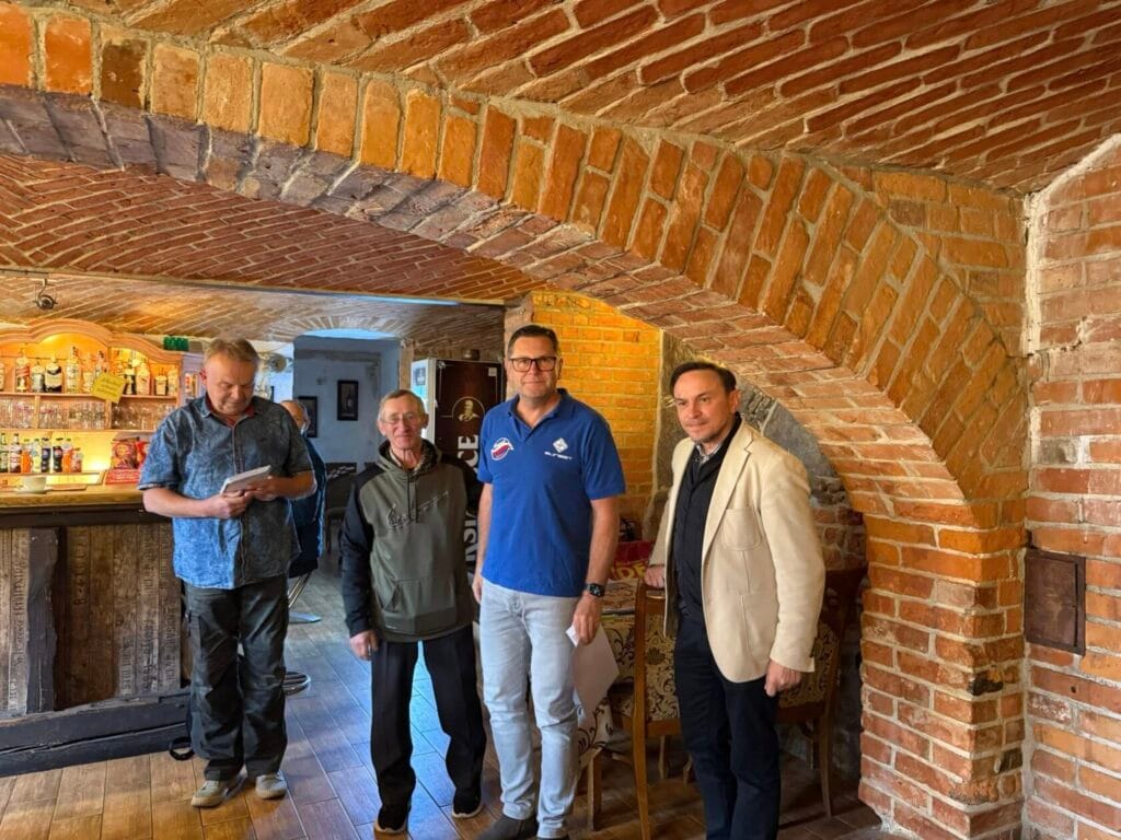 Czterech mężczyzn w ceglanych wnętrzach starej karczmy.