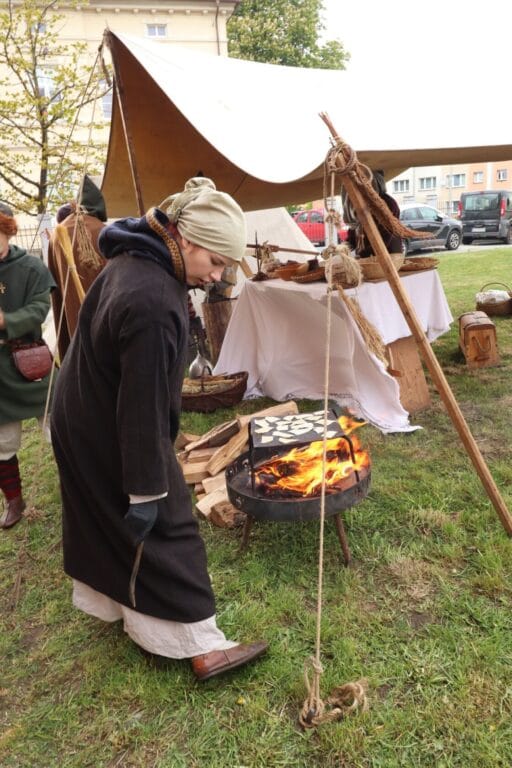Kobieta w historycznym stroju rozpala ognisko na festynie