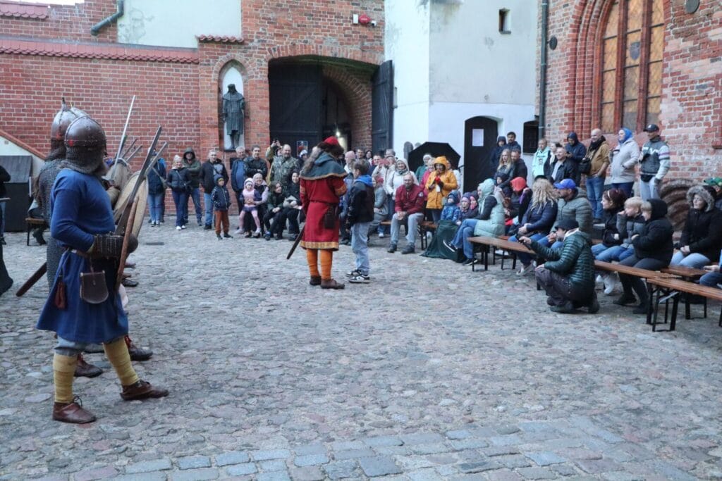 Rekonstrukcja historyczna na zamku, widzowie obserwują rycerzy.
