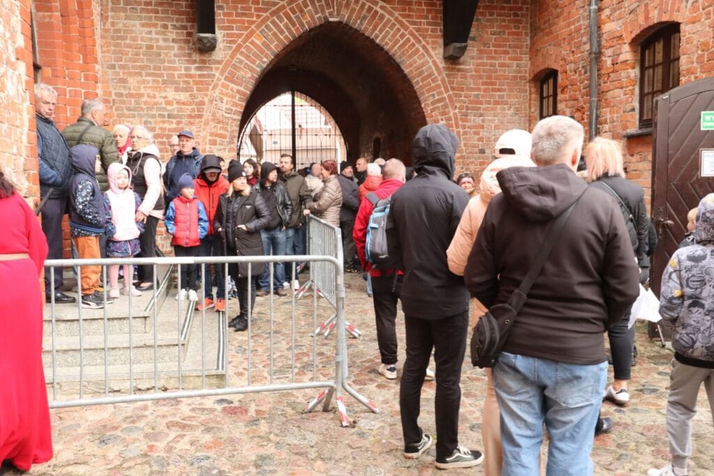 Grupa ludzi czeka przy bramie zamkowej