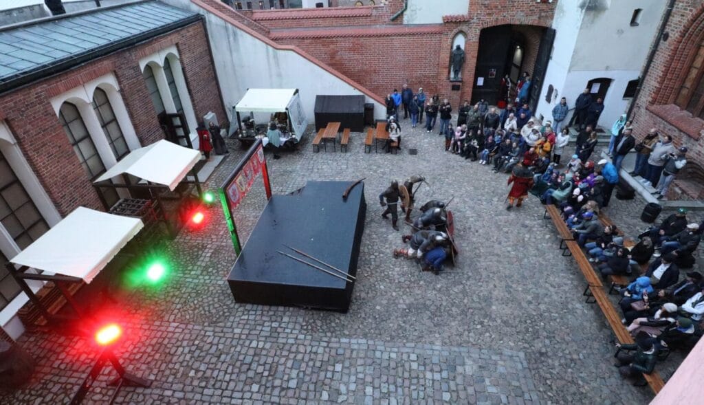 Widzowie oglądają pokaz teatralny na zamkowym dziedzińcu