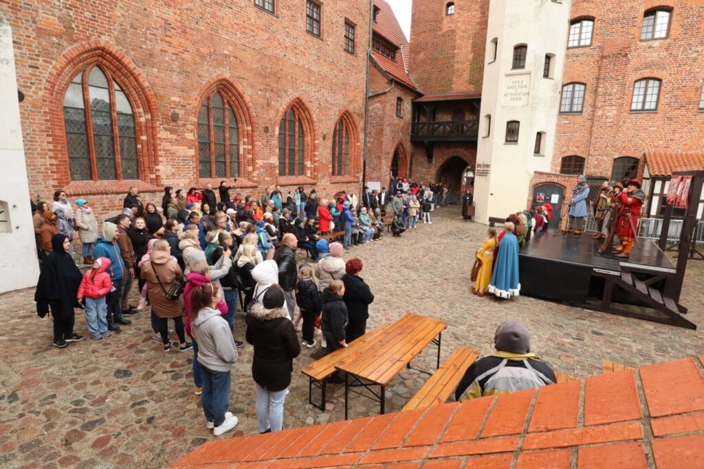Widzowie oglądają średniowieczne przedstawienie na zamkowym dziedzińcu
