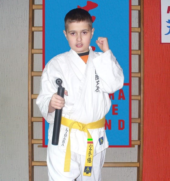 Chłopiec w karate gi z żółtym pasem trzyma nunchaku