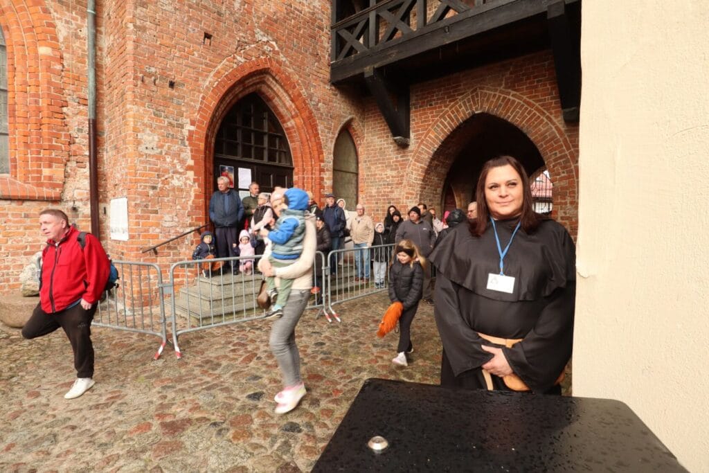 Osoby wychodzące z ceglanego kościoła, przewodniczka na pierwszym planie