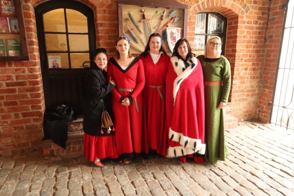 Kobiety w historycznych strojach stoją przed kamienną ścianą