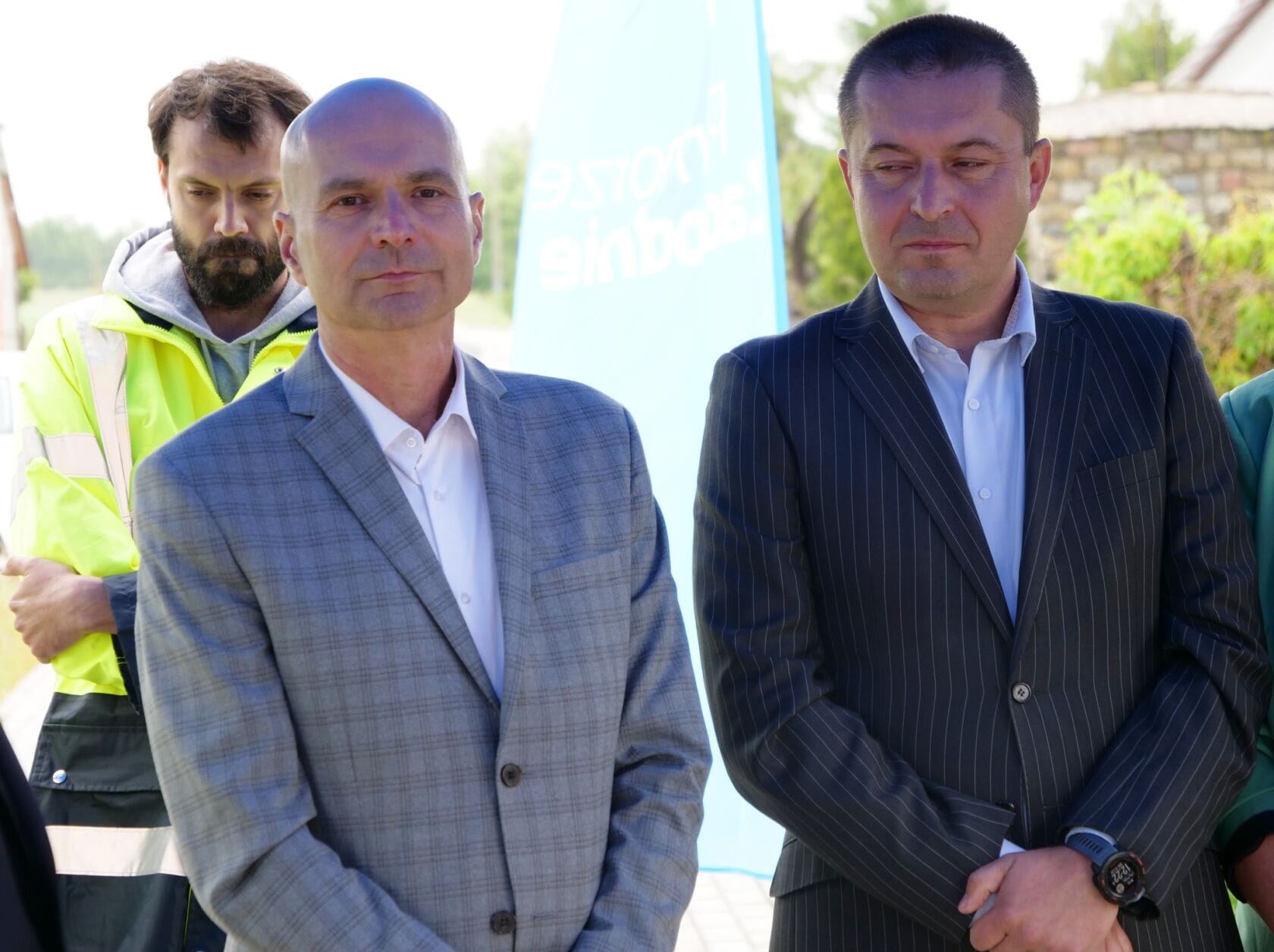 504005530_1117108270442896_8953968456791408022_n Trzej mężczyźni w garniturach na zewnątrz przy banerze