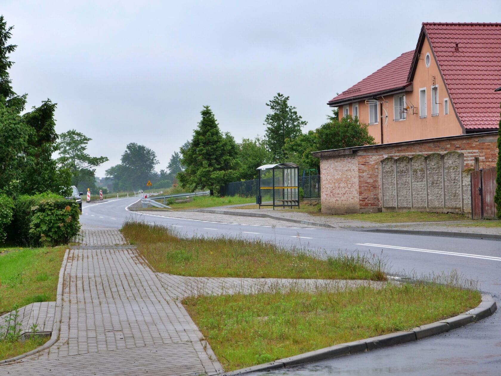 Chodnik i mokra droga przy domu, przystanek autobusowy