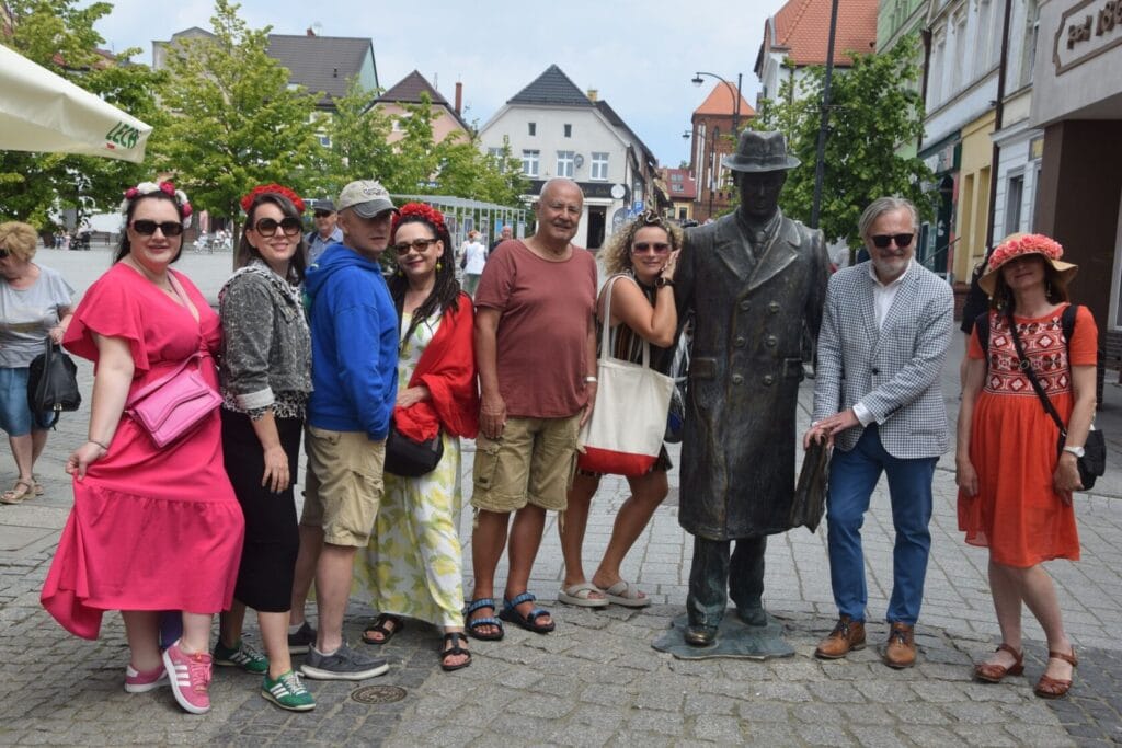 Grupa ludzi z pomnikiem w miejskim otoczeniu