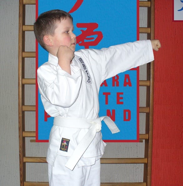 Chłopiec w karate-gi wykonuje cios pięścią