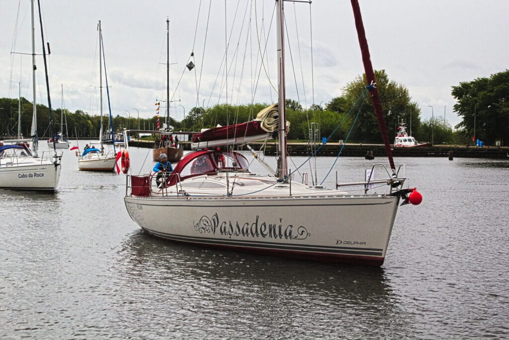 Jachty na rzece, ludzie na pokładzie, chmury nad drzewami