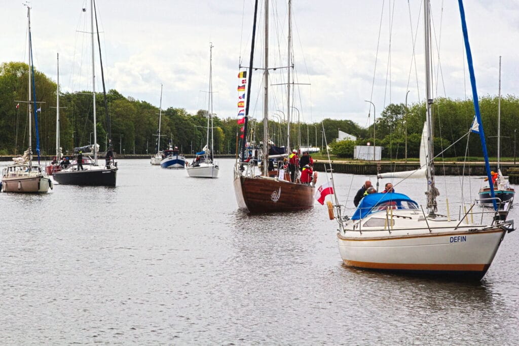 Łodzie z żaglami na spokojnej rzece, drzewa w tle