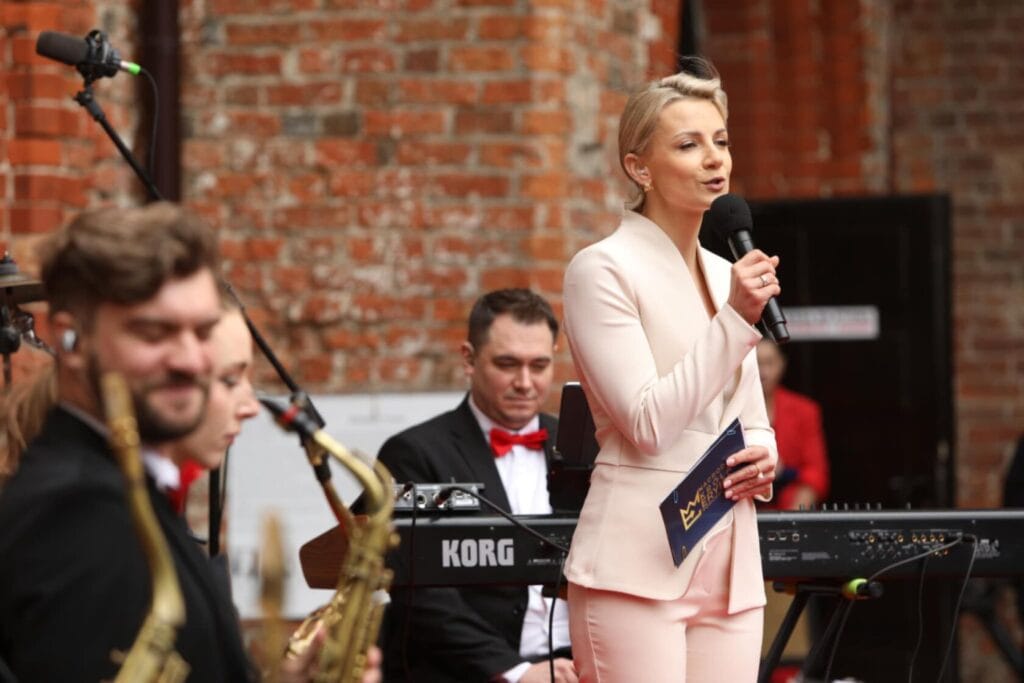 Kobieta śpiewa z zespołem na tle ceglanej ściany