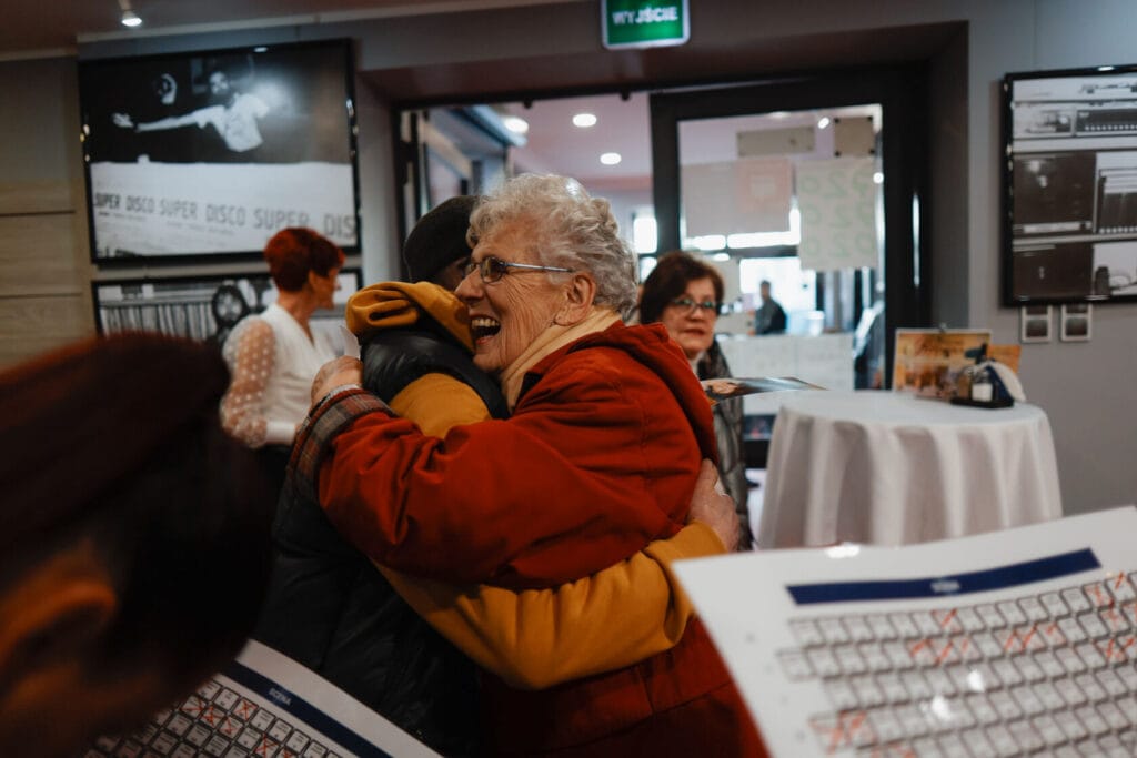 Starsza kobieta przytula mężczyznę w pomieszczeniu publicznym