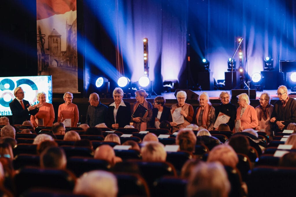 Seniorzy uczestniczą w wydarzeniu na scenie teatralnej