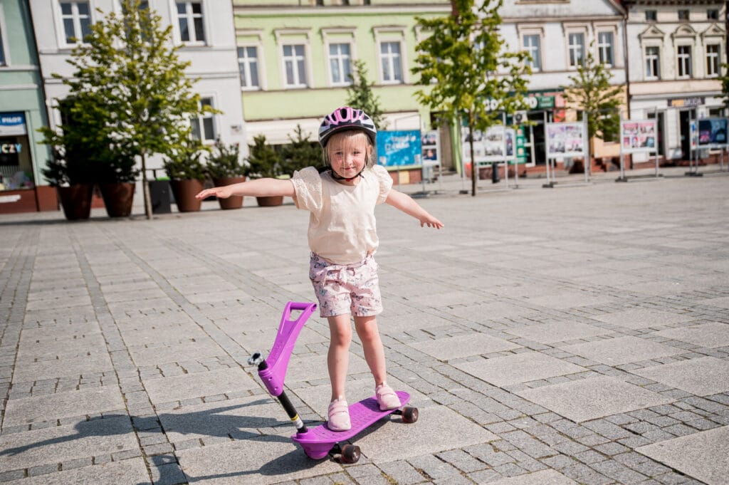 Dziewczynka z hełmem balansuje na hulajnodze w mieście.