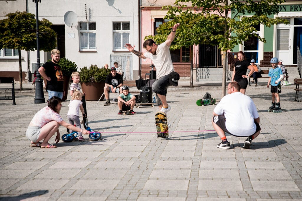 Mężczyzna wykonuje trik na deskorolce, otoczony obserwatorami.