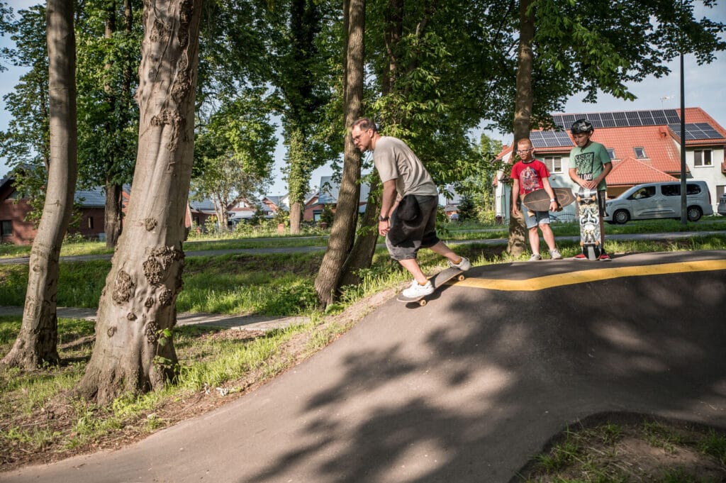 Mężczyzna jeździ na deskorolce, dzieci obserwują w parku