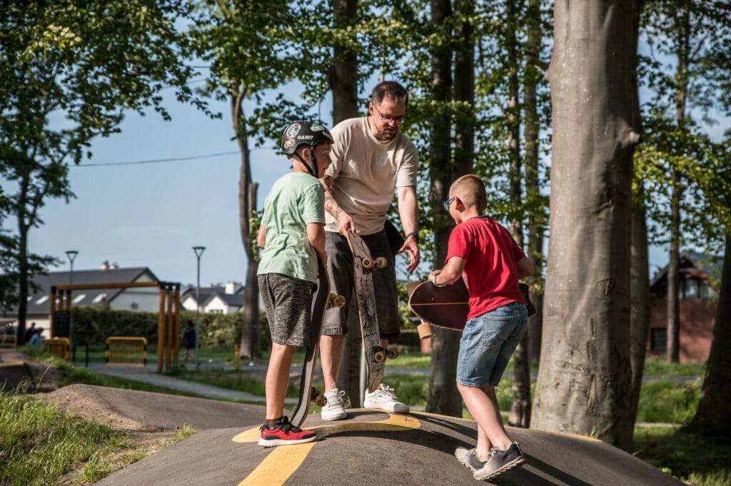 Dorosły uczy dzieci jeździć na deskorolce w parku