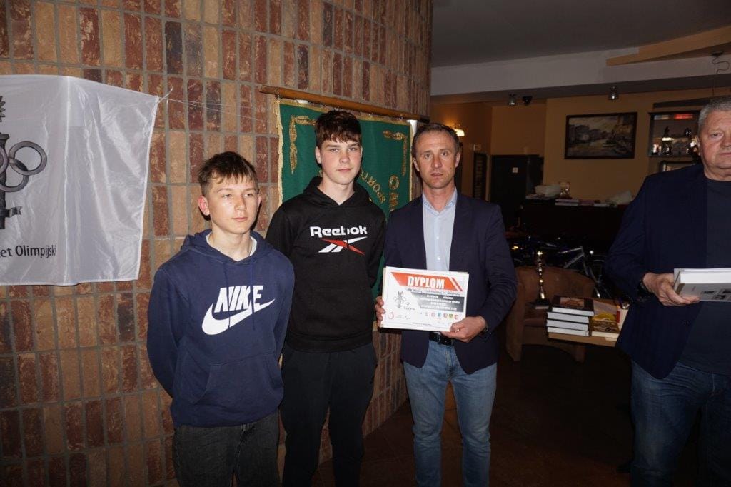 Trzy osoby przyznają nagrody młodym sportowcom w pomieszczeniu