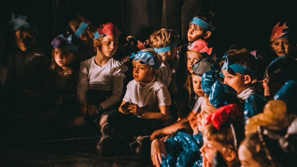 Dzieci z opaskami zwierząt oglądają przedstawienie