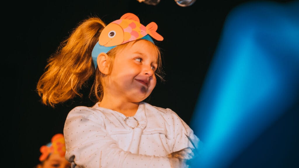 Dziewczynka w opasce z rybką śmieje się na scenie