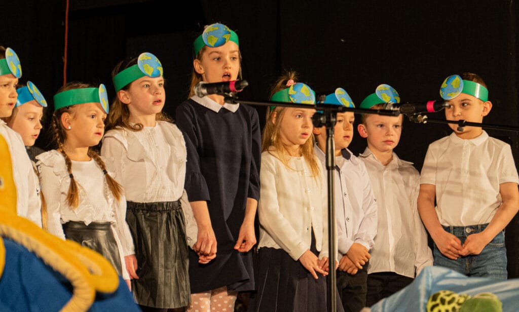 Dzieci w opaskach z globusem śpiewają na scenie