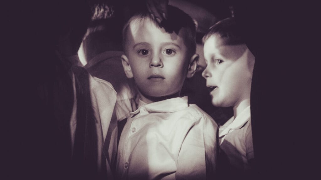 Chłopiec w białej koszuli otoczony innymi dziećmi.