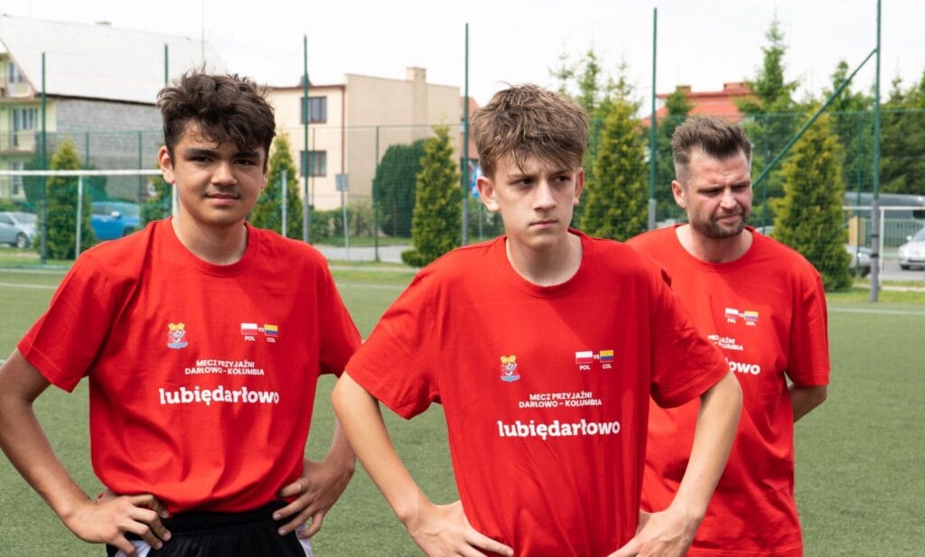 Trzej piłkarze w czerwonych koszulkach na boisku