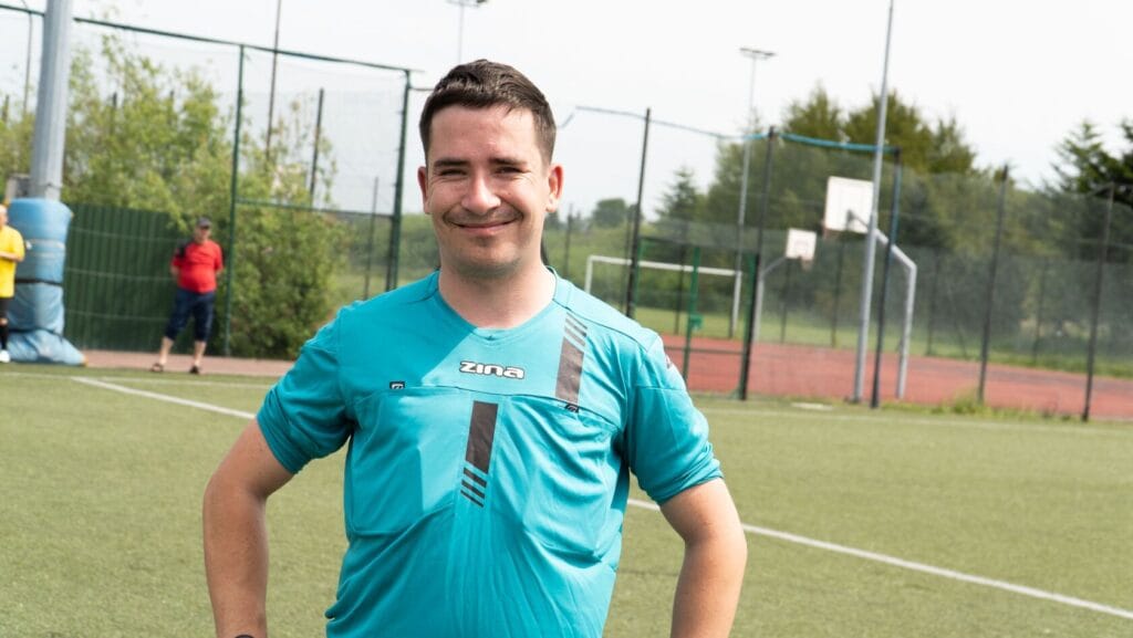 Uśmiechnięty mężczyzna w turkusowej koszulce na boisku