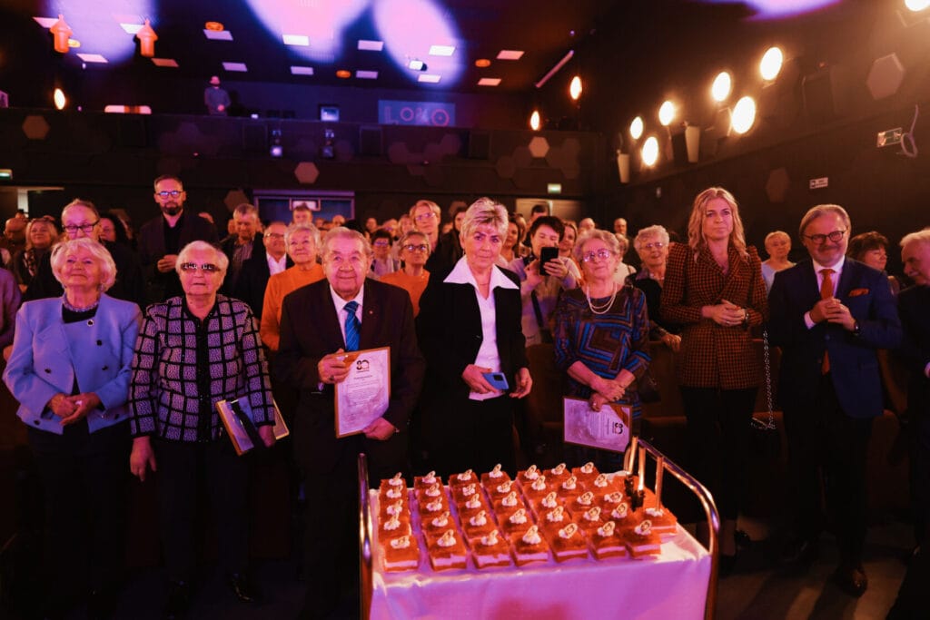 Grupa osób ogląda wydarzenie w zaciemnionej sali