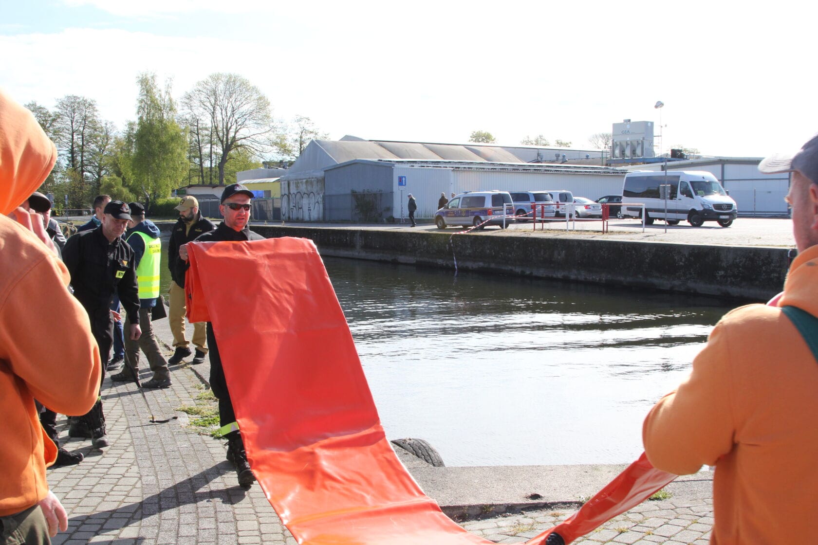 IMG_0197 Osoby pracujące z pomarańczową barierą na brzegu rzeki