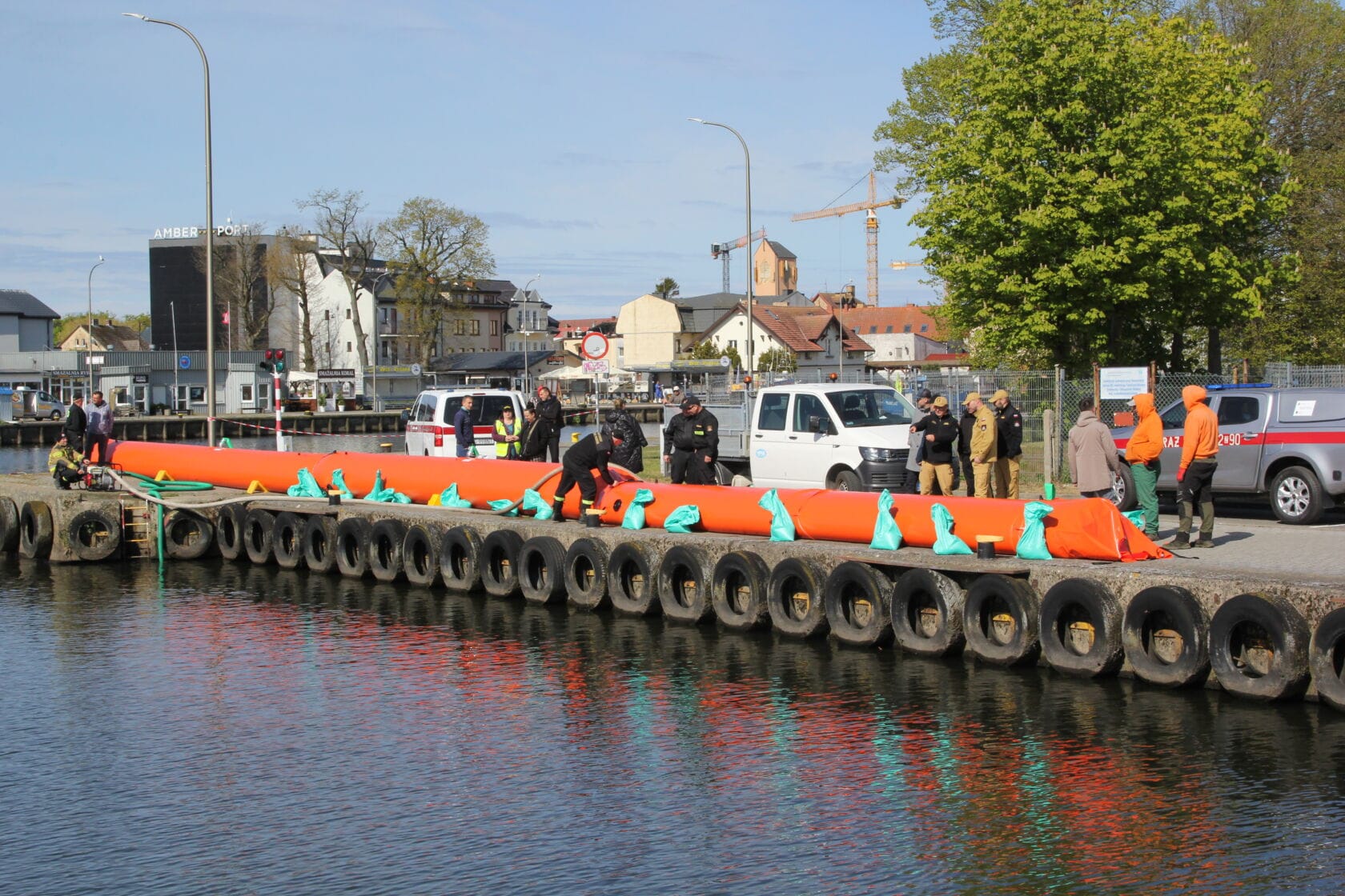 Pracownicy przygotowują pomarańczową barierę olejową na nabrzeżu